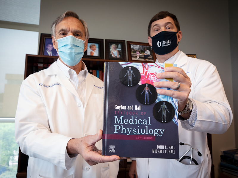 Dr. John Hall and Dr. Michael hall holding up a copy of the Textbook of Medical Physiology